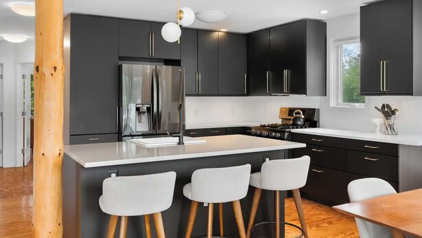 Una cocina moderna con armarios oscuros, un refrigerador de acero inoxidable y una isla central con taburetes de bar.