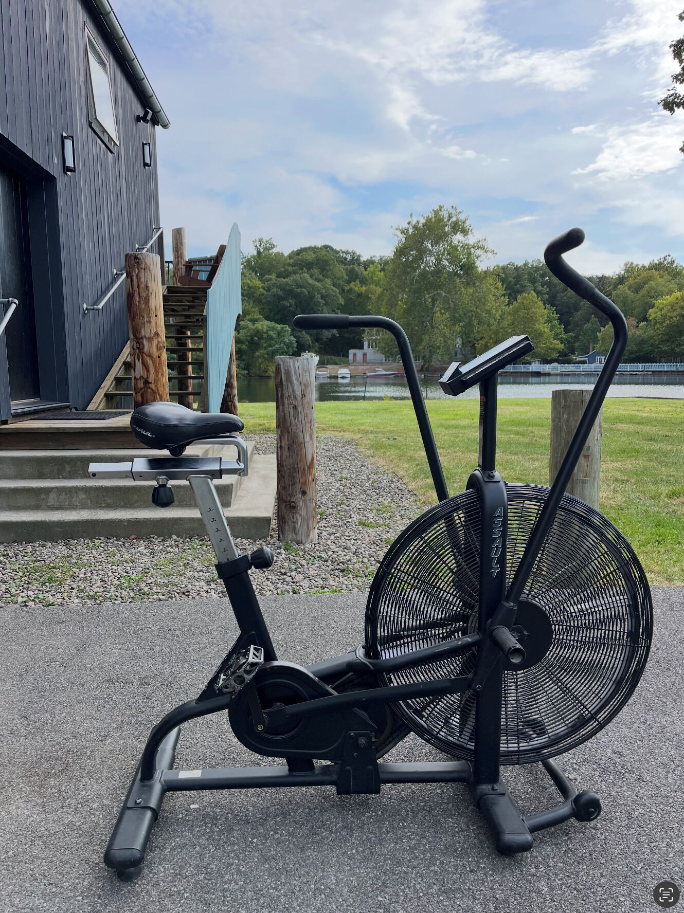 An outdoor exercise machine with a fan and a seat, positioned on a paved area with steps leading to a building.