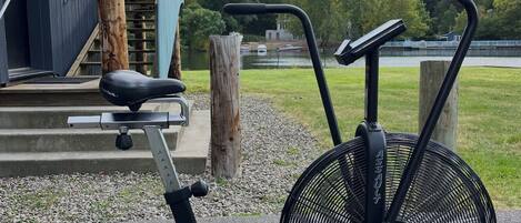 An outdoor exercise machine with a fan and a seat, positioned on a paved area with steps leading to a building.