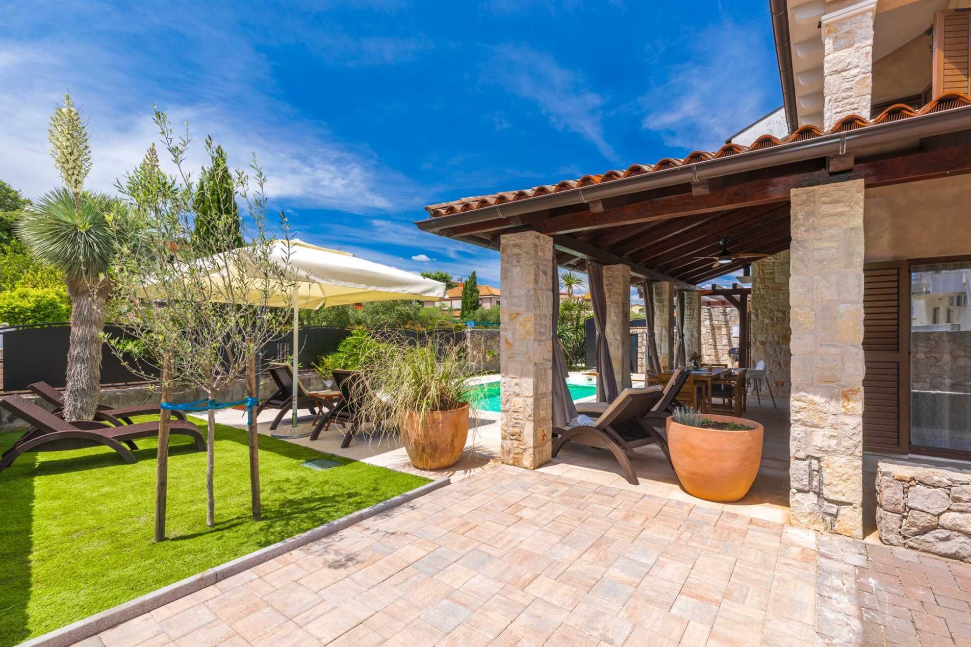 A covered patio area with a pool, outdoor seating, and a well-maintained lawn.