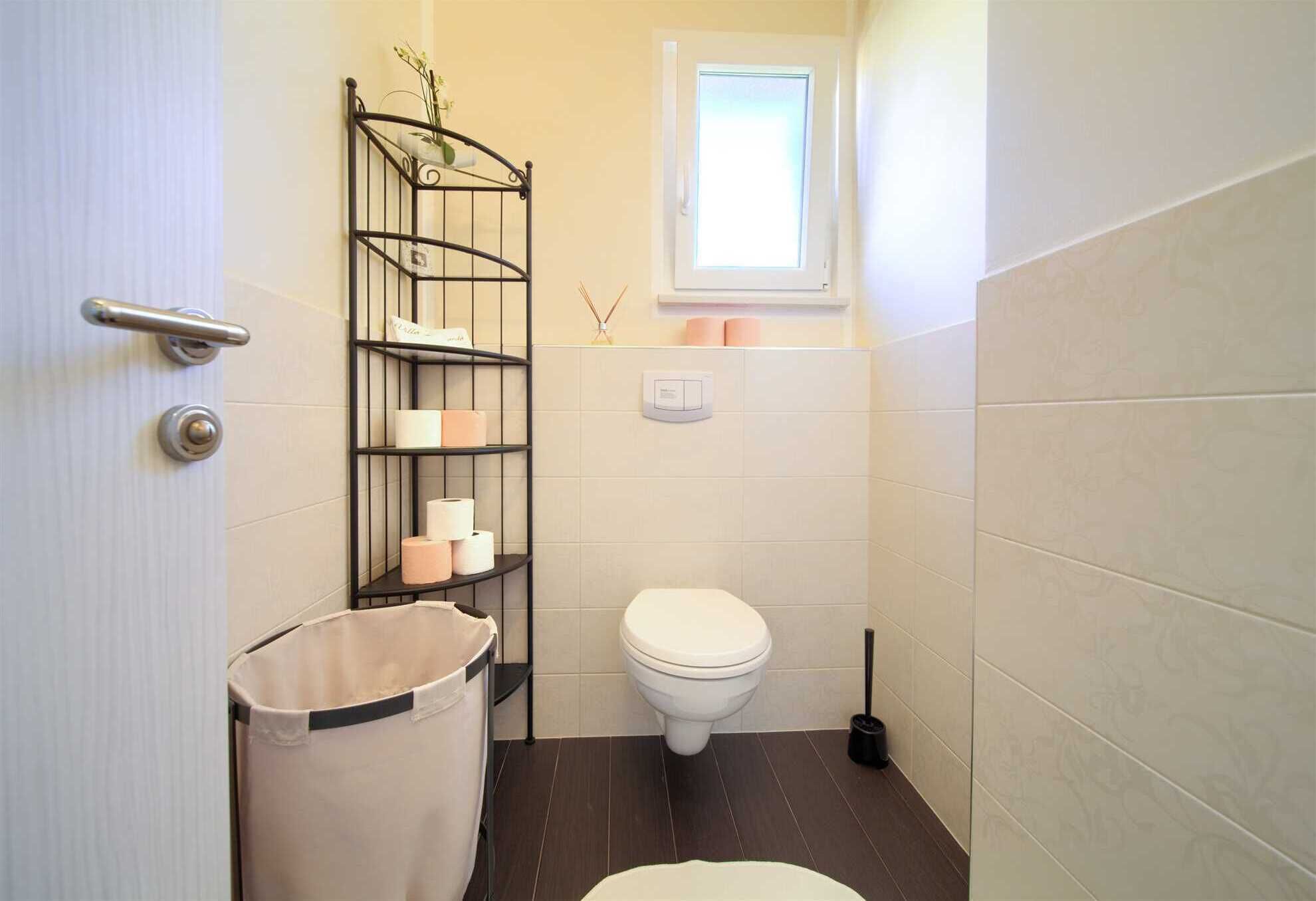 A compact bathroom with a toilet, a shelf with toiletries, a window, and a door.