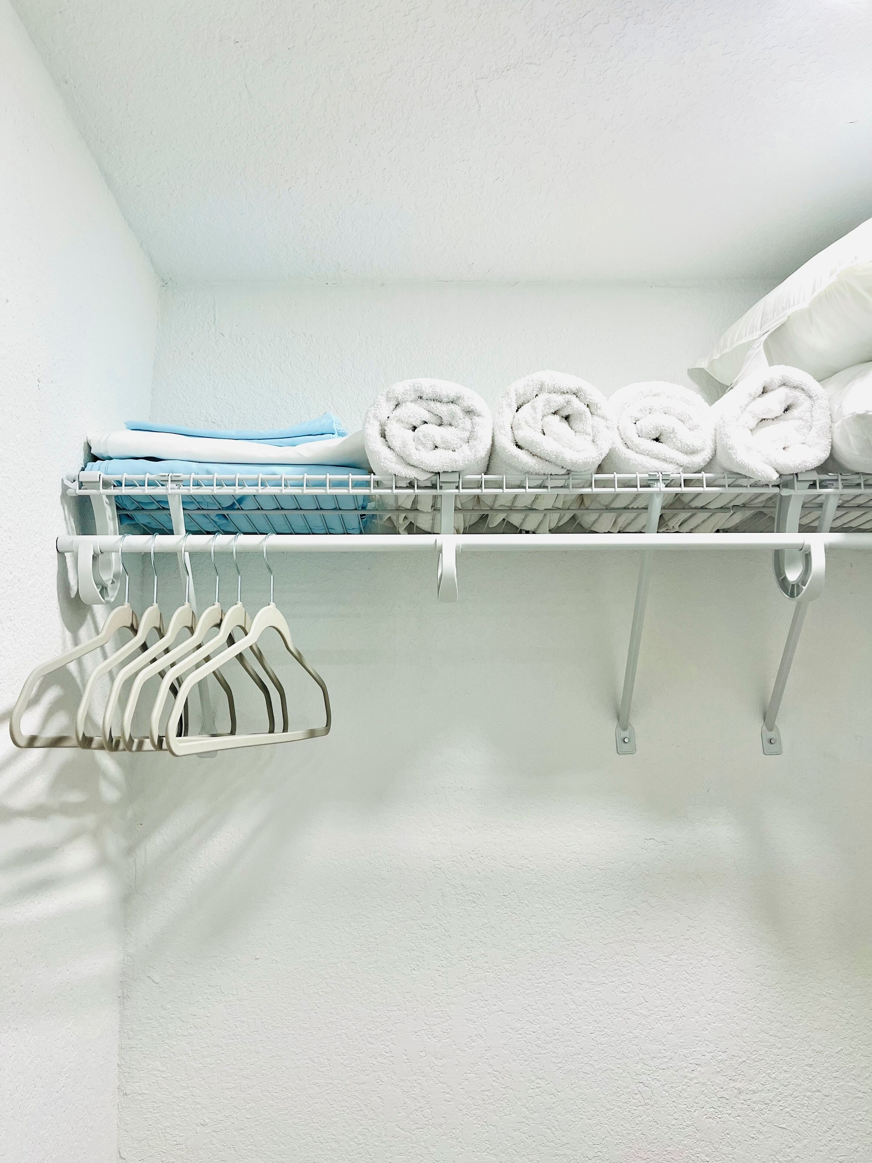 A white closet with neatly folded towels and a rack of white hangers.