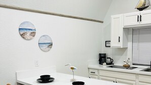 Een moderne keuken met witte kasten, een wit eiland met twee barstoelen en decoratieve wanddecoratie.