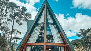 A triangular wooden structure with glass windows and two wooden chairs outside. - Recanto Lavi (Urubici)