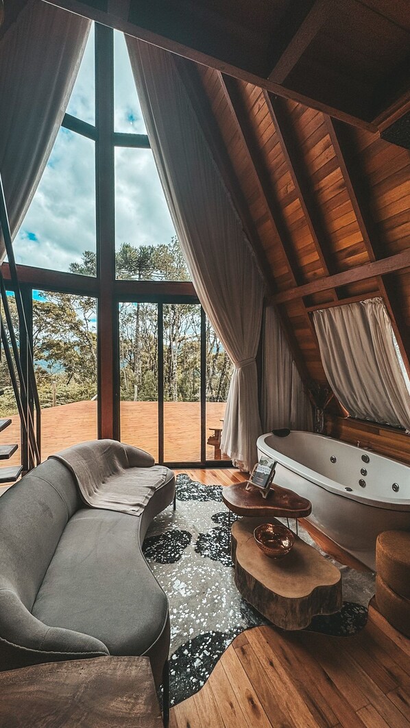 A room with a large window, a sofa, a bathtub, and a wooden table.