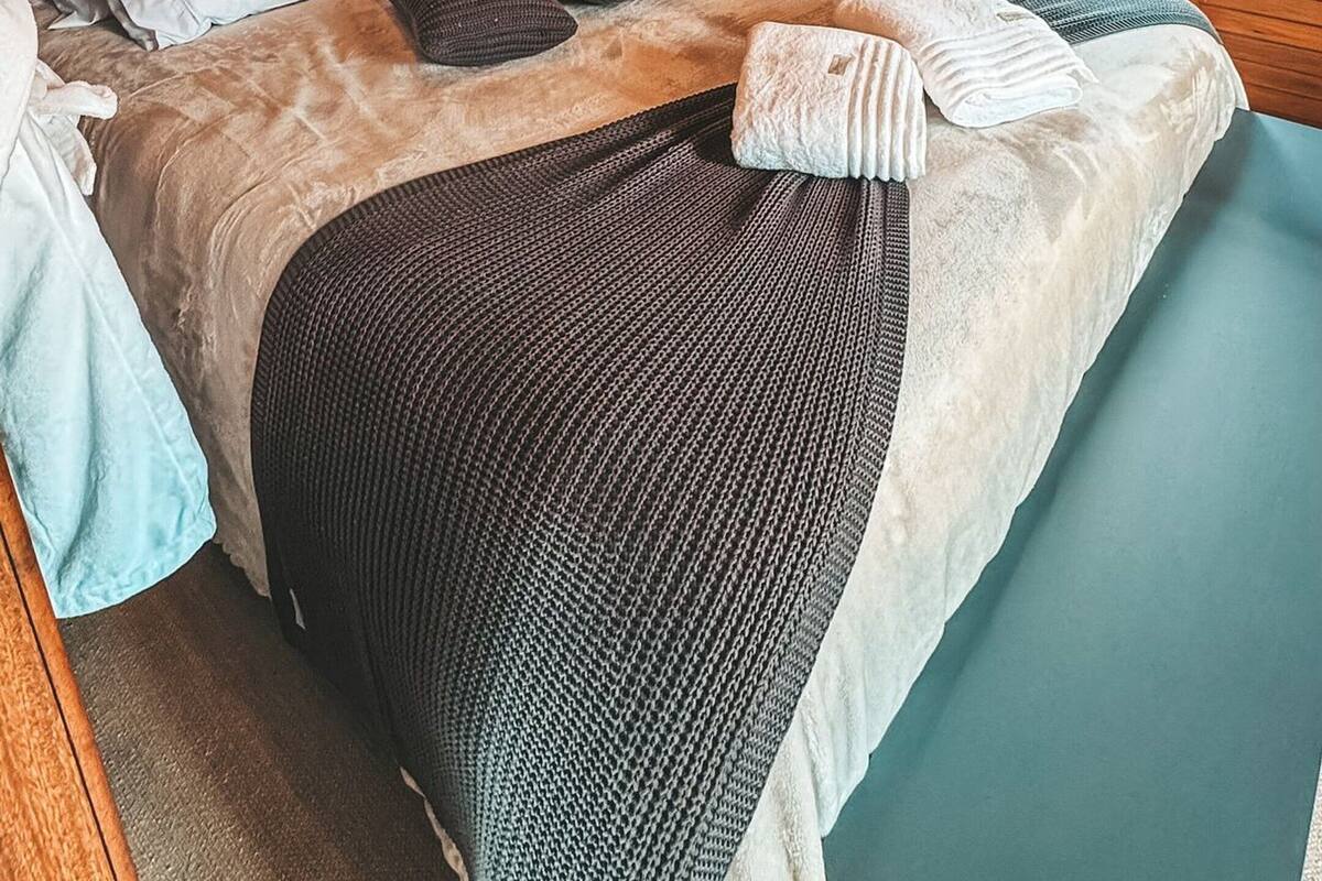 A wooden ceiling, a bed with pillows and a blanket, and a window with curtains.
