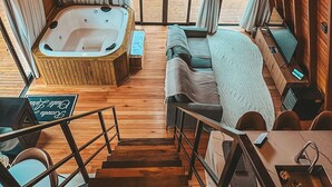 A cozy cabin interior with a wooden ceiling, a hot tub, a sofa, and a dining area. - Recanto Lavi (Urubici)