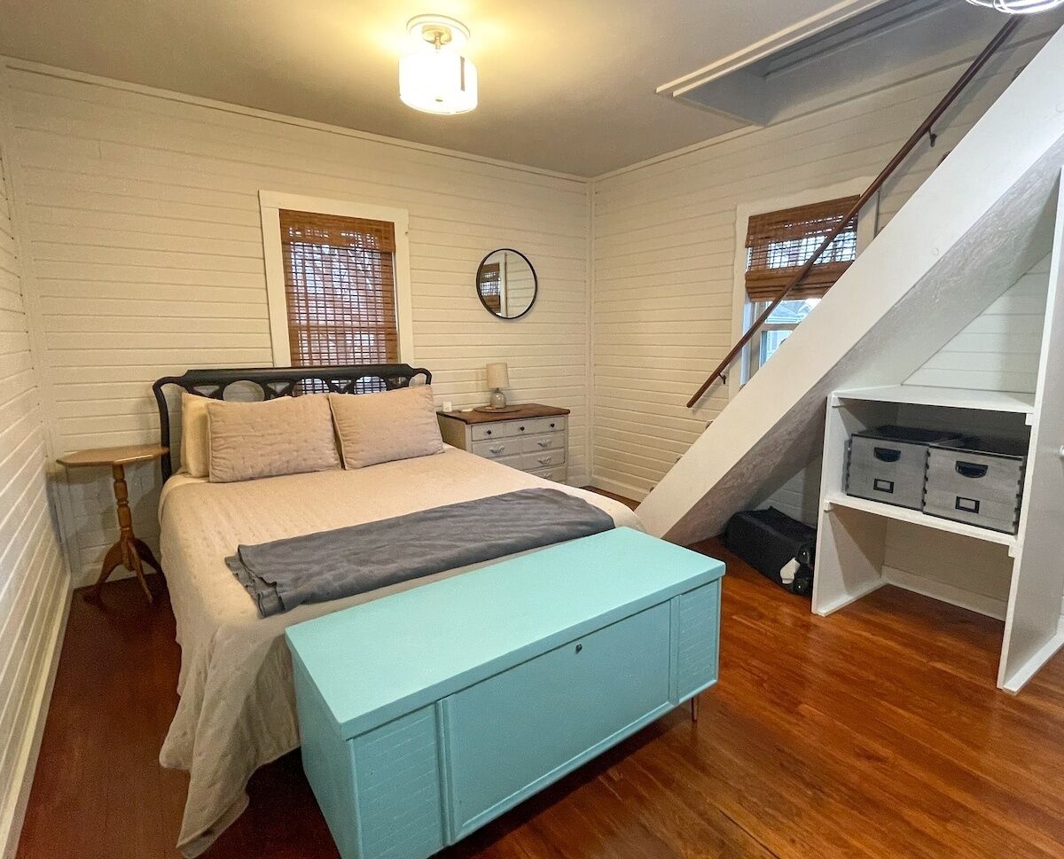 Een slaapkamer met een bed, nachtkastjes, een spiegel, een dressoir en een trap.