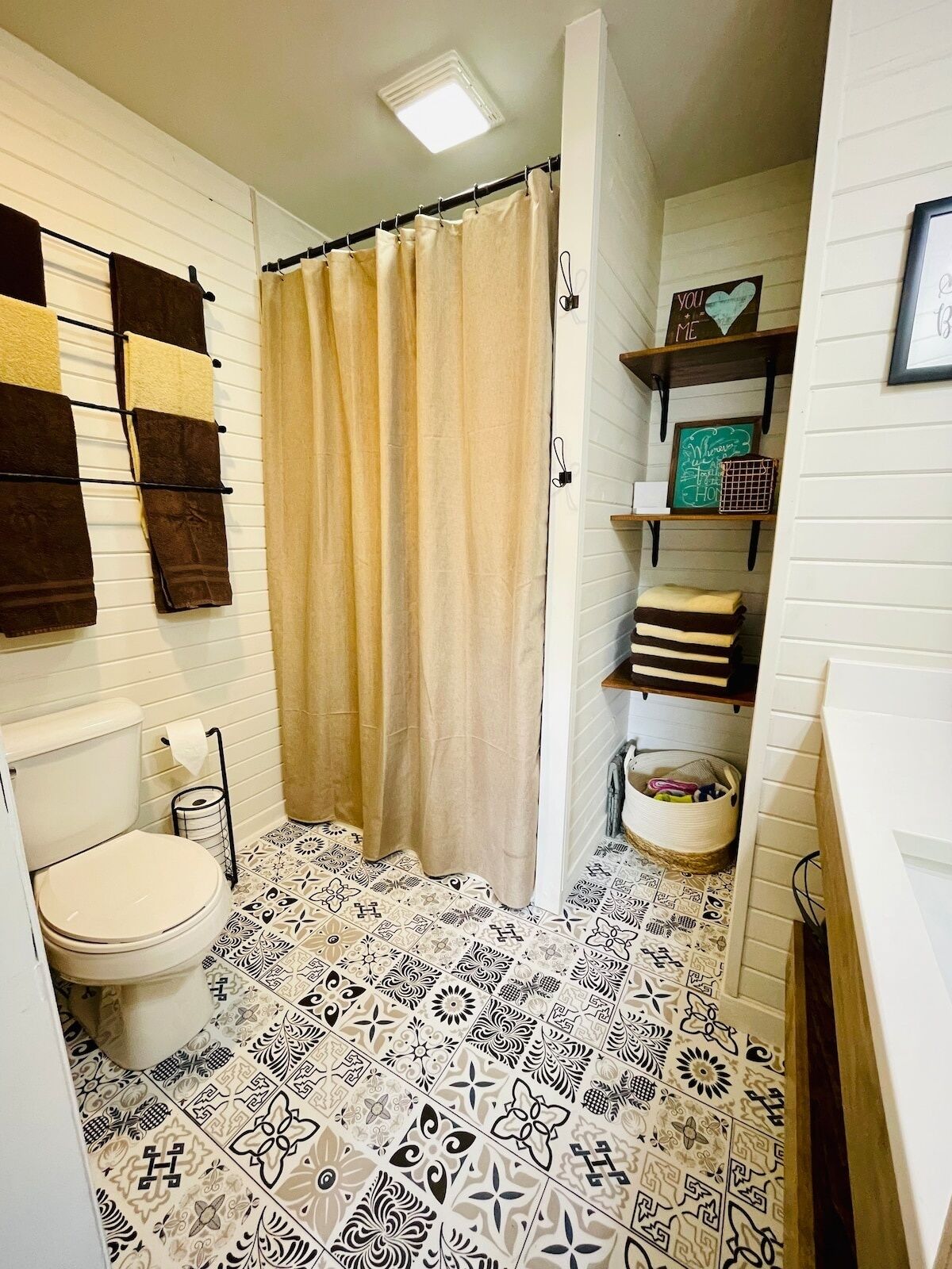A bathroom with a toilet, patterned floor tiles, a shower curtain, and towel racks.