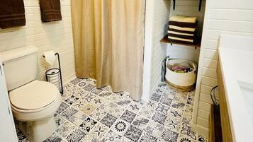 A bathroom with a toilet, patterned floor tiles, a shower curtain, and towel racks.