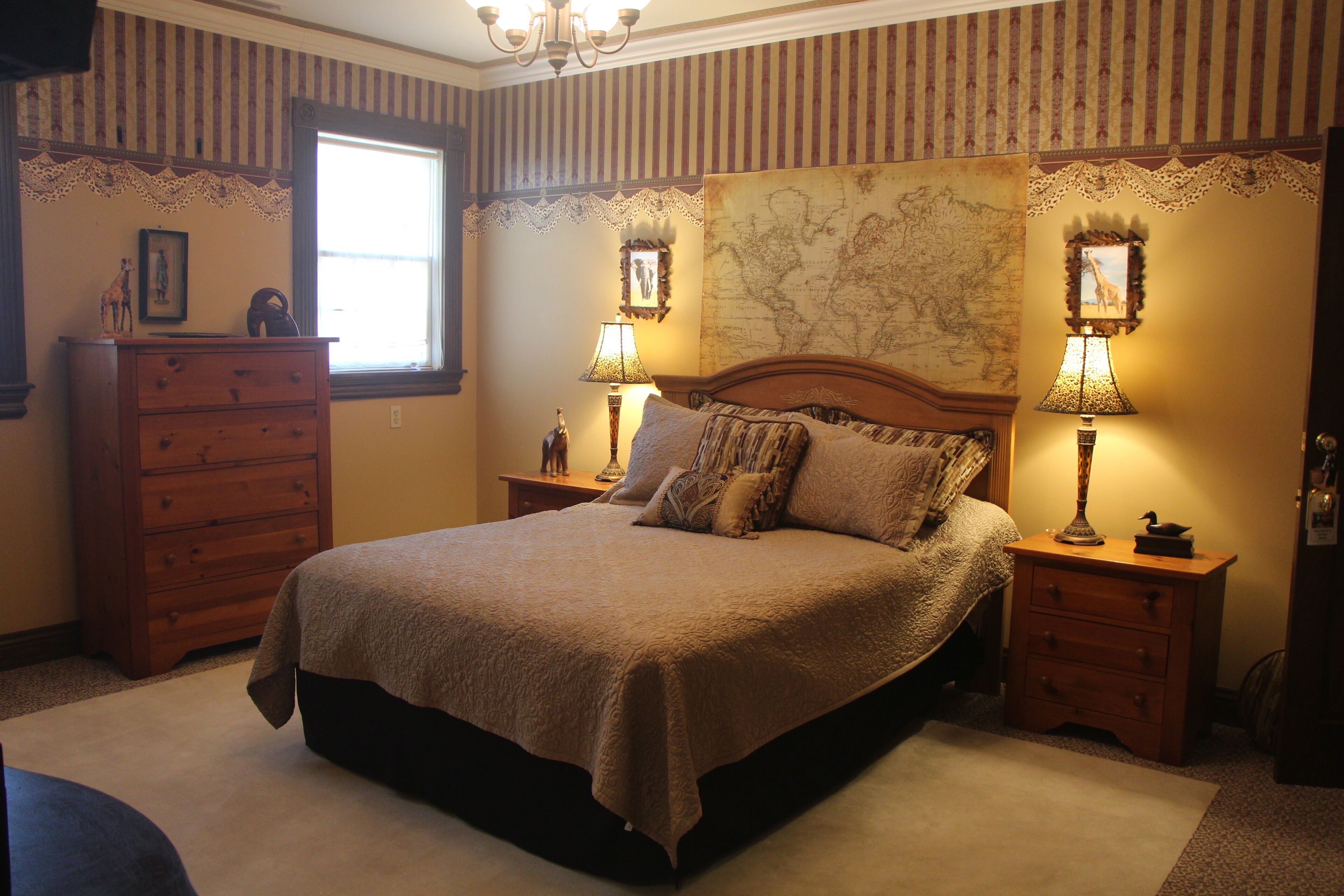 A bedroom with a large bed, two nightstands with lamps, a dresser, and a window with a view.