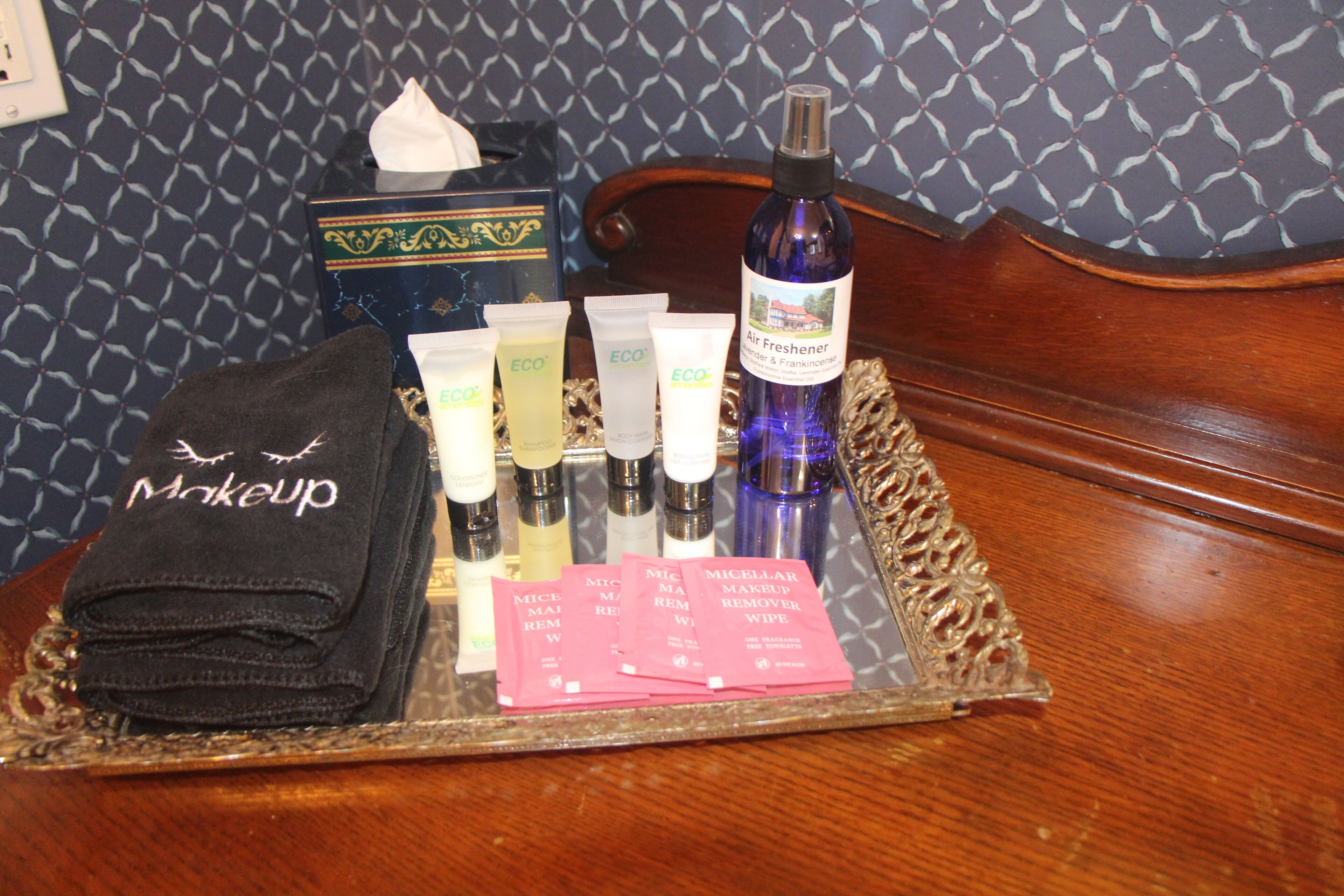 A tray with makeup items, a tissue box, and a bottle of air freshener on a wooden table.