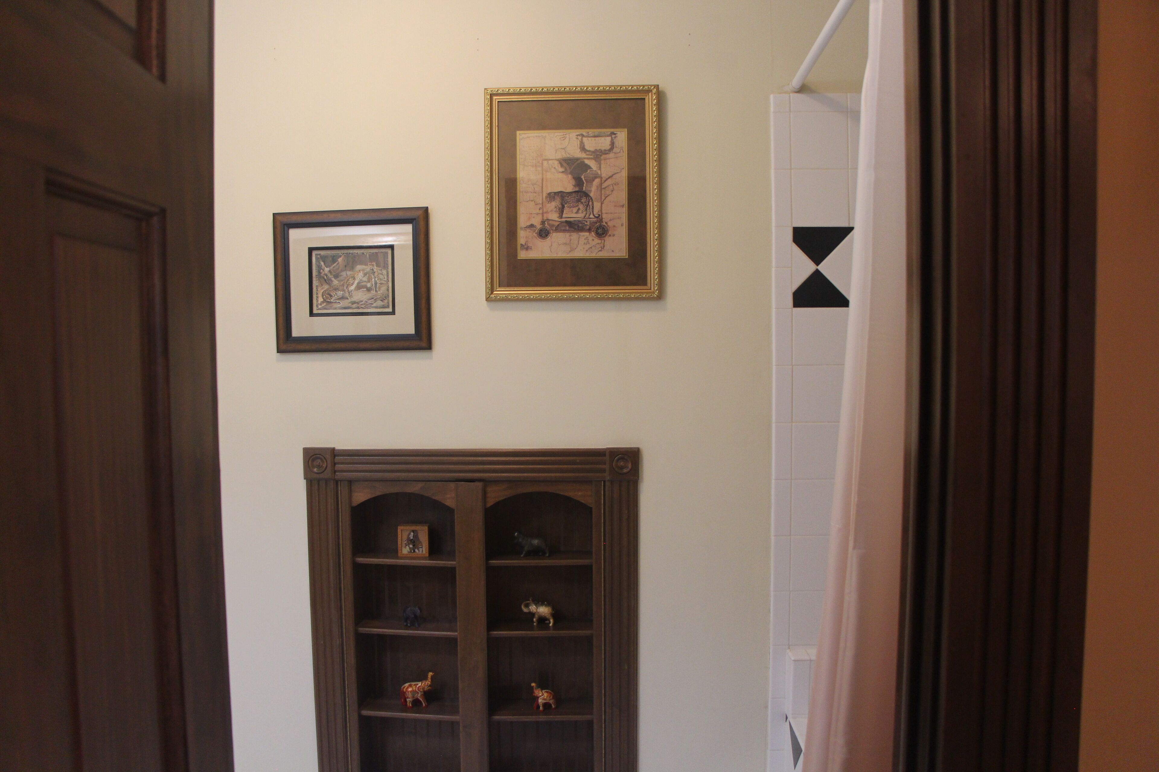 A hallway with a wooden door, a wall-mounted shelf with figurines, and two framed pictures.