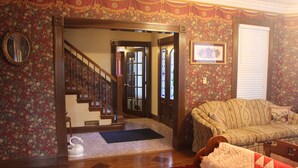Une pièce avec un papier peint à motifs floraux, un escalier en bois, un canapé et une couvre-lit matelassée.