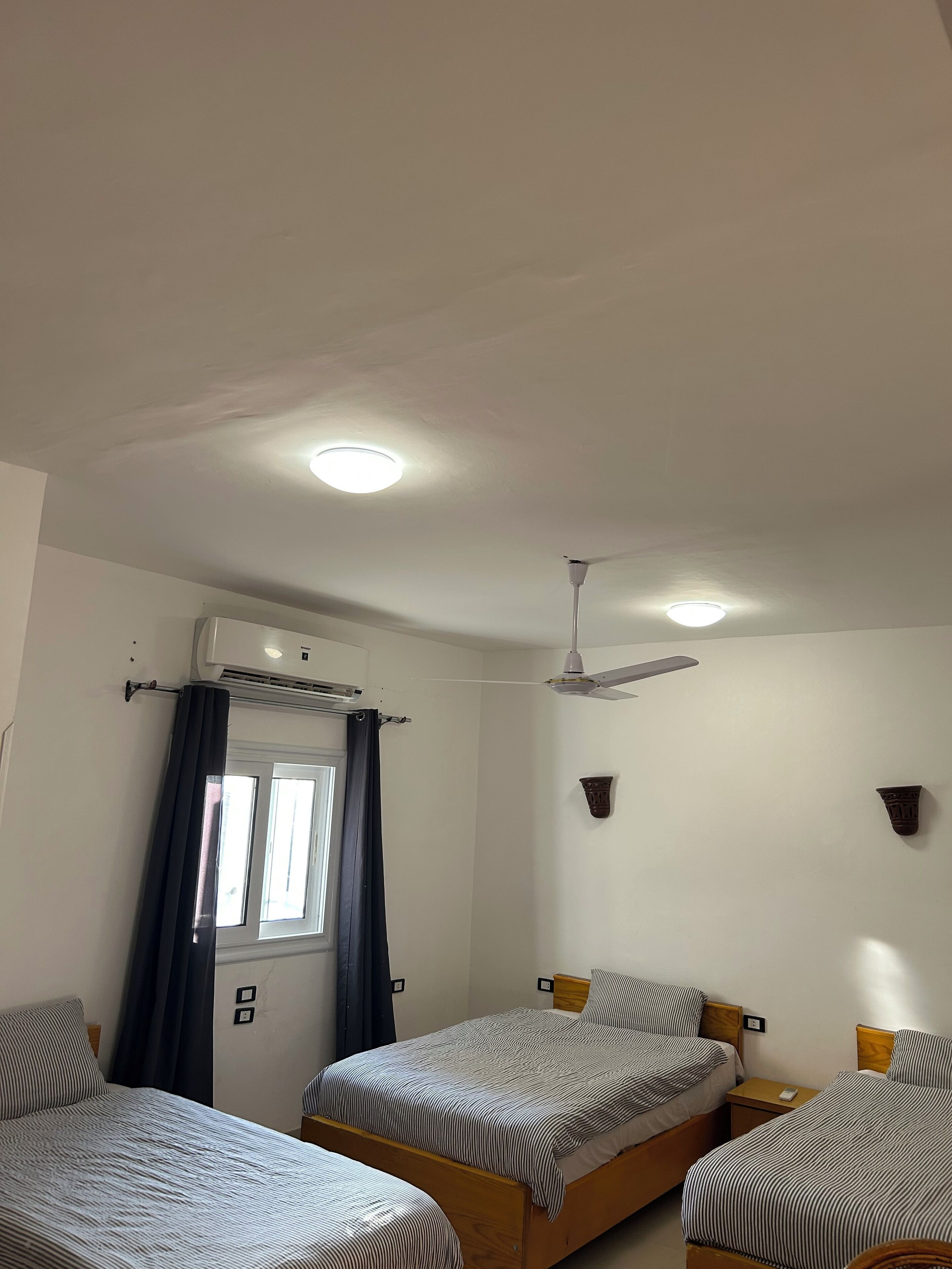 Un dormitorio con dos camas individuales, ventilador de techo, equipo de aire acondicionado y una ventana con cortinas.