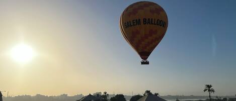 A hot air balloon with "Salem Balloons" written on it, flying over a rooftop area with lounge chairs and a pool.