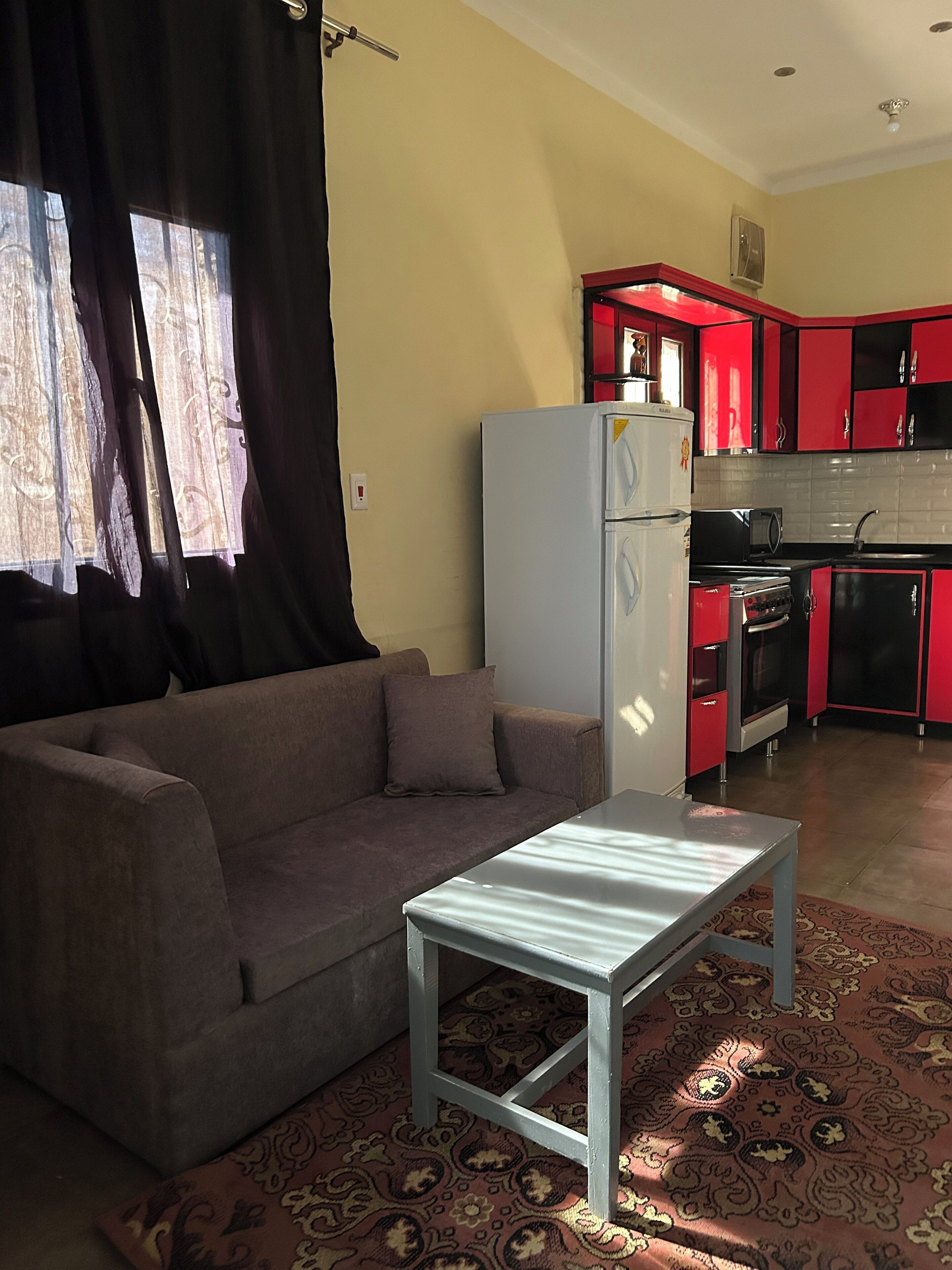 Ein Wohnzimmer mit Sofa und kleinem Tisch, eine Küche mit roten Schränken und einem gemusterten Teppich.