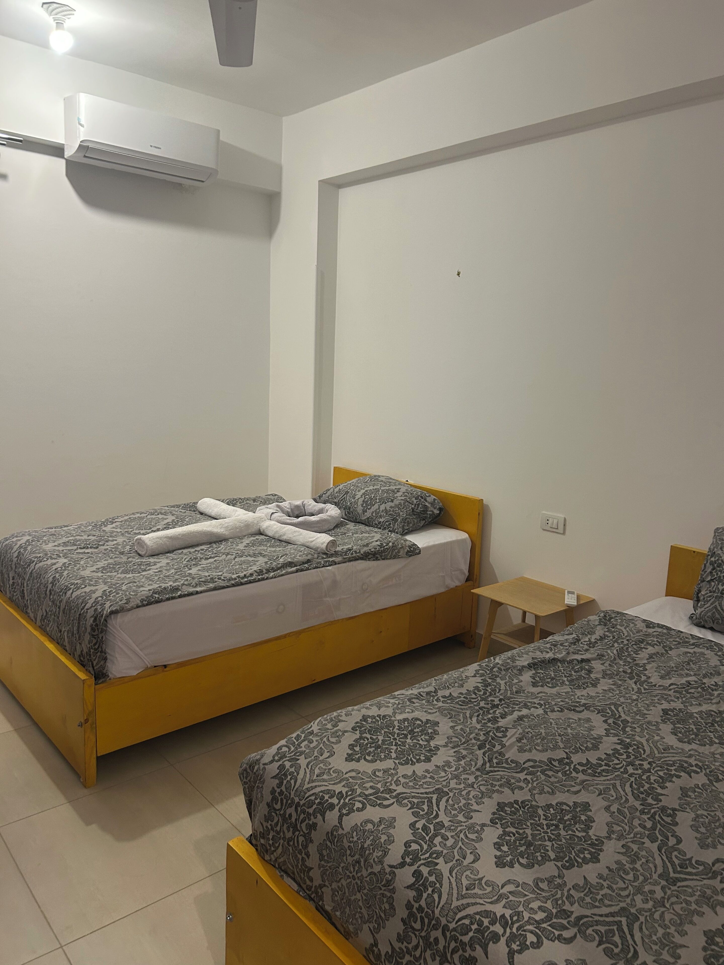 A bedroom with two beds, a small wooden nightstand, and an air conditioning unit on the wall.