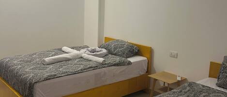A bedroom with two beds, a small wooden nightstand, and an air conditioning unit on the wall.