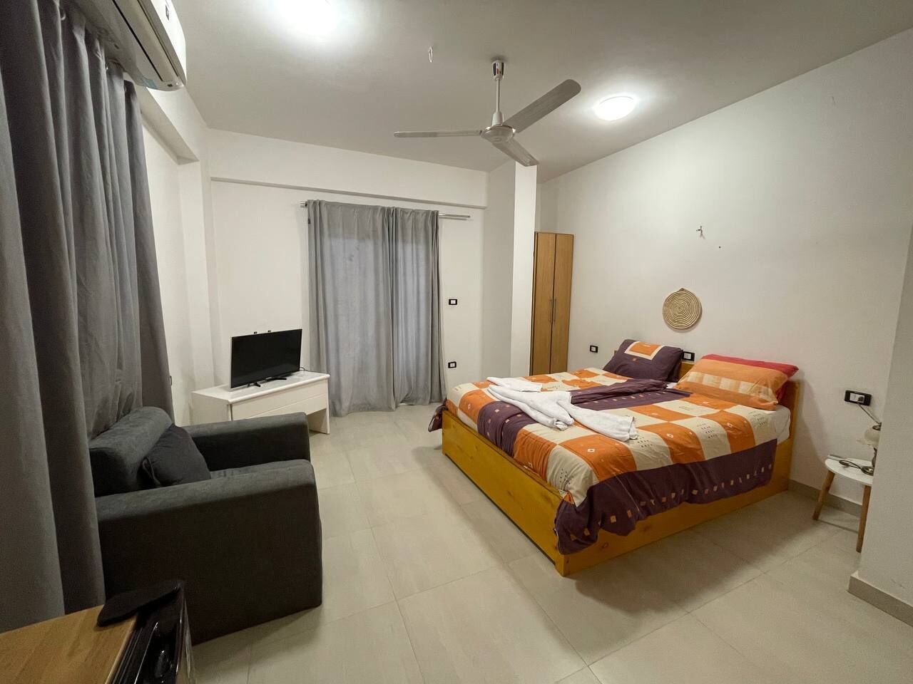 A bedroom with a bed, a desk, a chair, a television, and a ceiling fan.