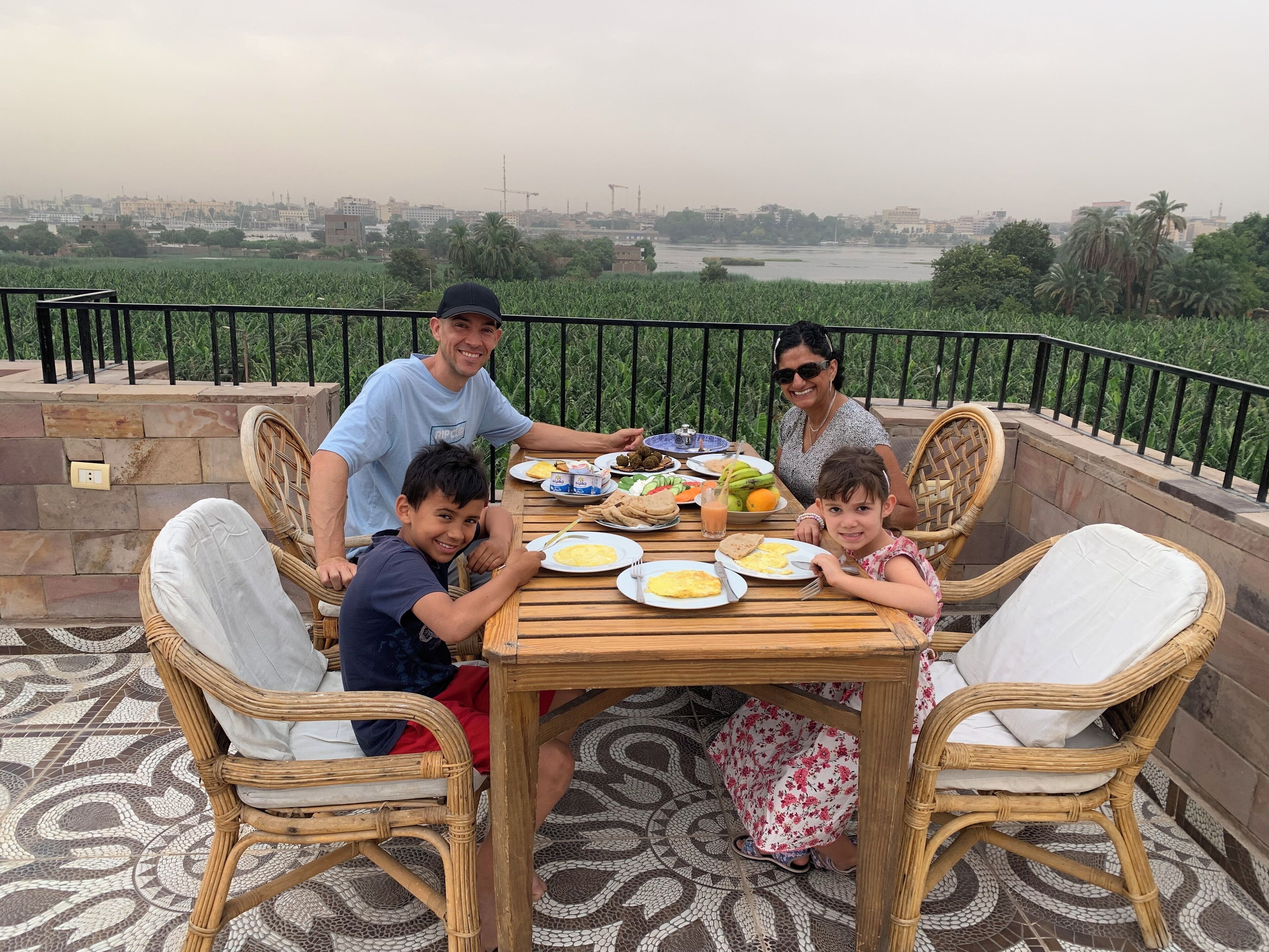 Una familia cenando al aire libre con vistas a un paisaje urbano y un río.