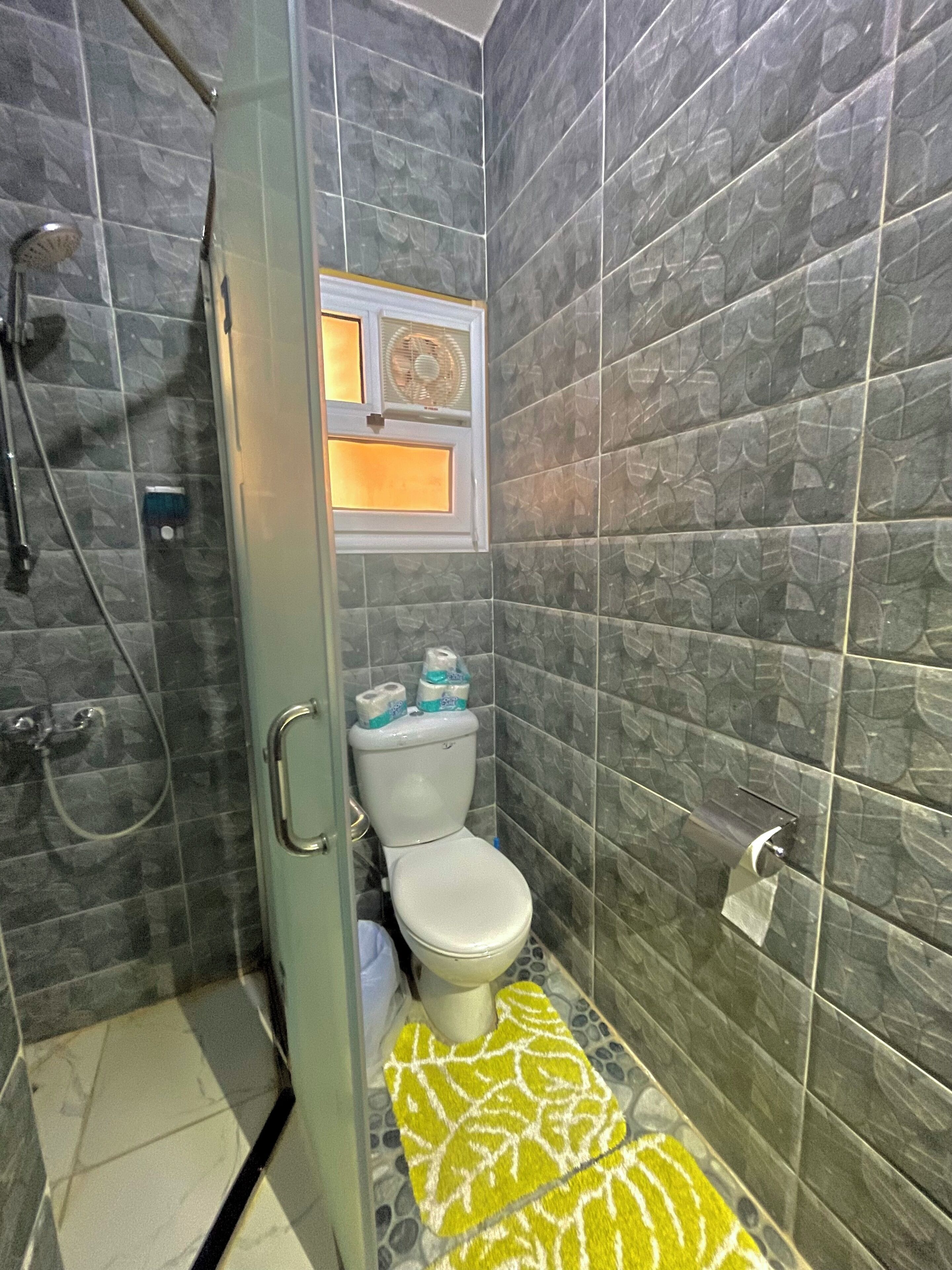A small bathroom with a toilet, a shower, and a window above the toilet.