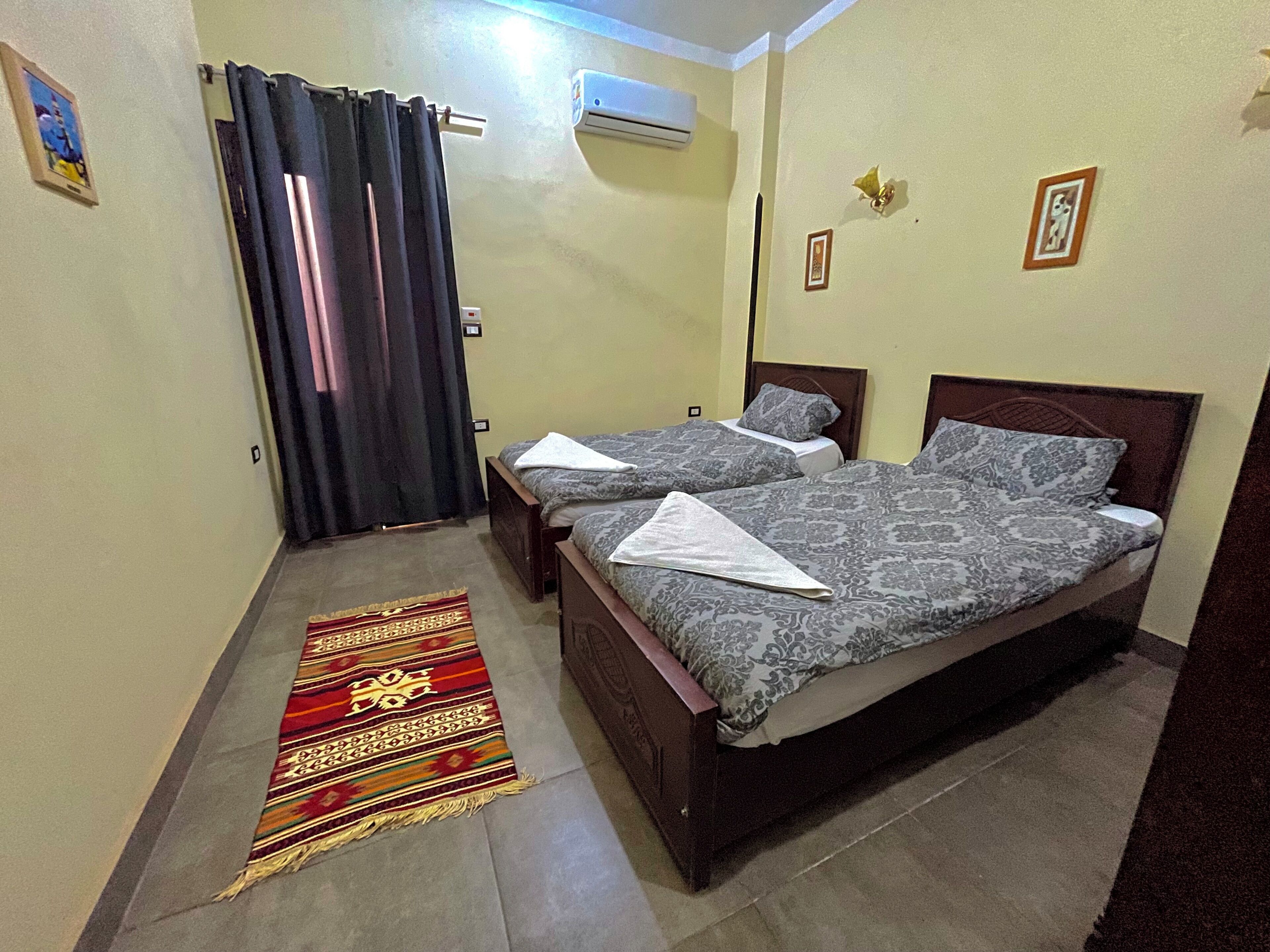 Una habitación con dos camas, un tapete estampado, una cortina y un equipo de aire acondicionado.