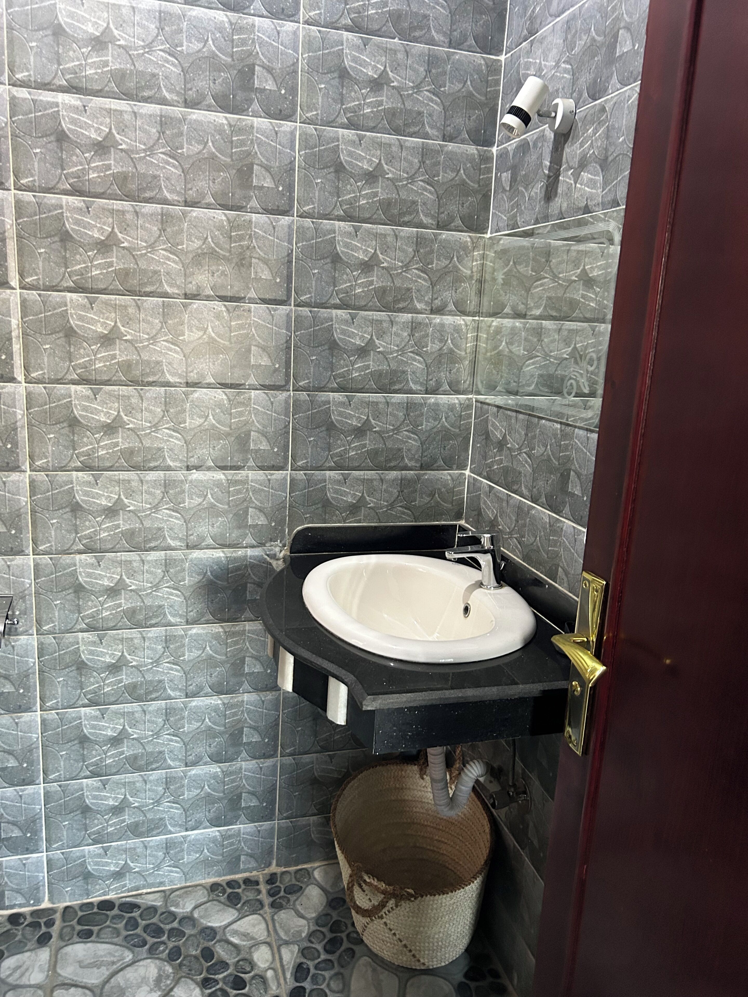 A bathroom with a white sink, dark tiles, and a shower head.
