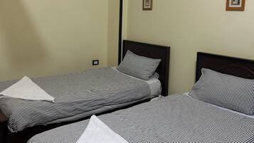 A hotel room with two beds, a ceiling fan, an air conditioning unit, and two framed pictures on the wall.