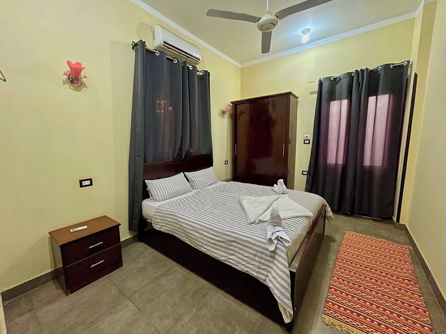 A bedroom with a bed, a wardrobe, a nightstand, and a ceiling fan.