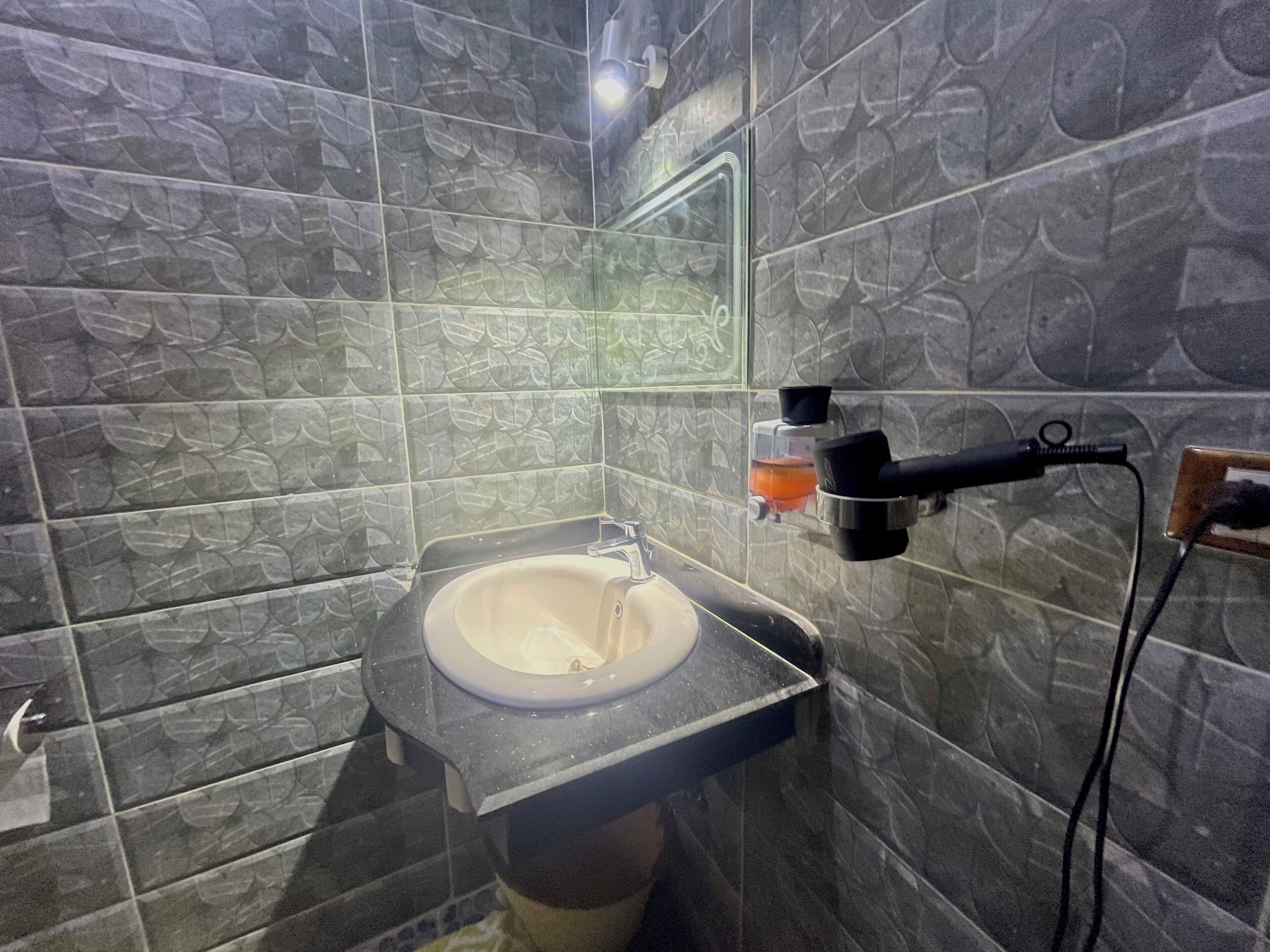 Un baño con lavamanos, un espejo y un secador de pelo fijado a la pared.