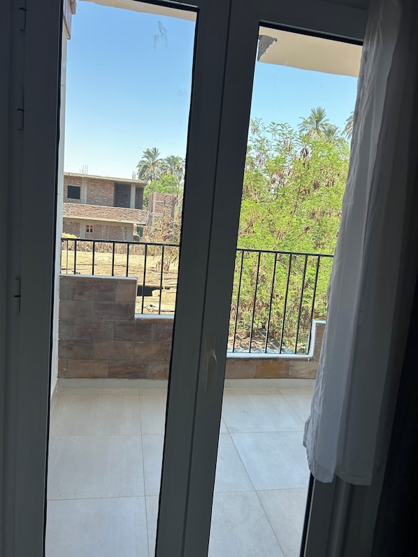 A view from a balcony with a metal railing, a stone wall, and a building in the background. - Nile Panorama Hotel & Restaurant (Luxor)