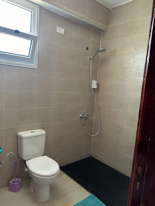 Un baño con inodoro, ducha y ventana.