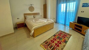 A bedroom with a bed, a TV, a ceiling fan, a window with curtains, and a patterned rug. - Nile Panorama Hotel & Restaurant (Luxor)