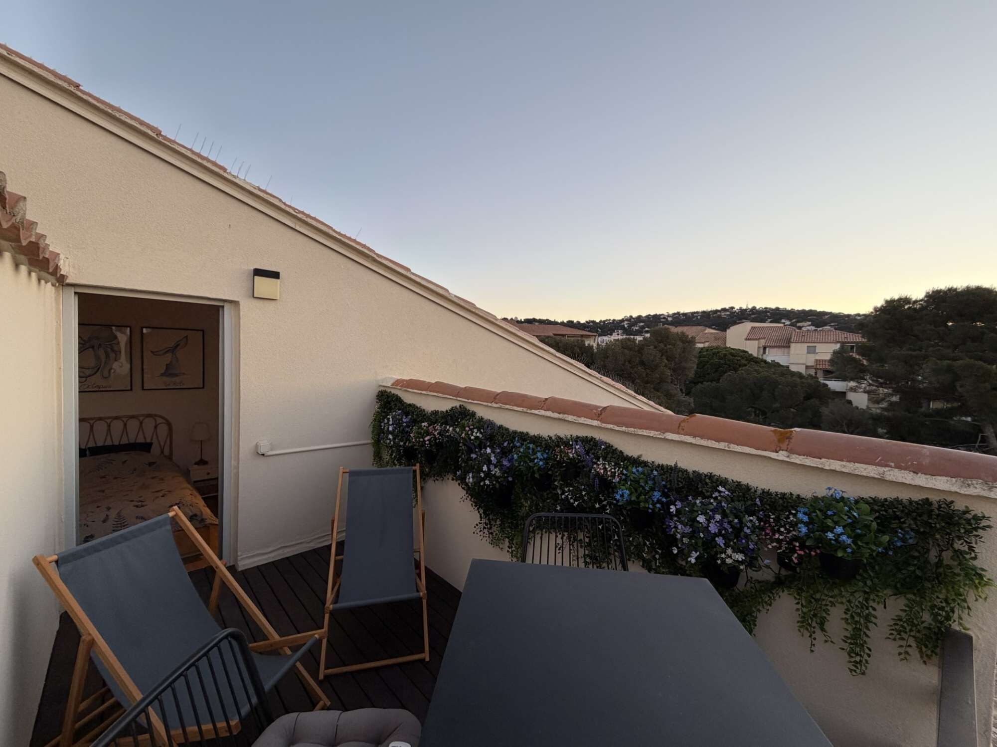 Une terrasse sur le toit offrant une vue sur le paysage environnant, un petit coin salon avec des chaises et une porte donnant accès à un espace intérieur.