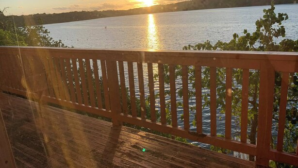 Eine Holzterrasse mit Blick auf einen ruhigen See, im Hintergrund ein Sonnenuntergang.