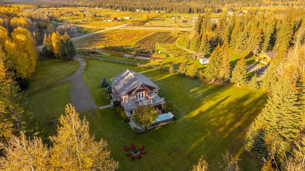Una casa grande con un césped cuidado y una piscina, rodeada de un bosque denso y campos abiertos.