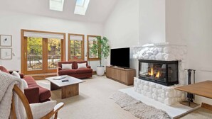 A spacious living room with a fireplace, comfortable seating, and large windows.