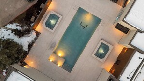 Ein Luftbild eines Hotels mit einem zentralen Schwimmbecken, zwei kleineren Pools und einer verschneiten Landschaft.