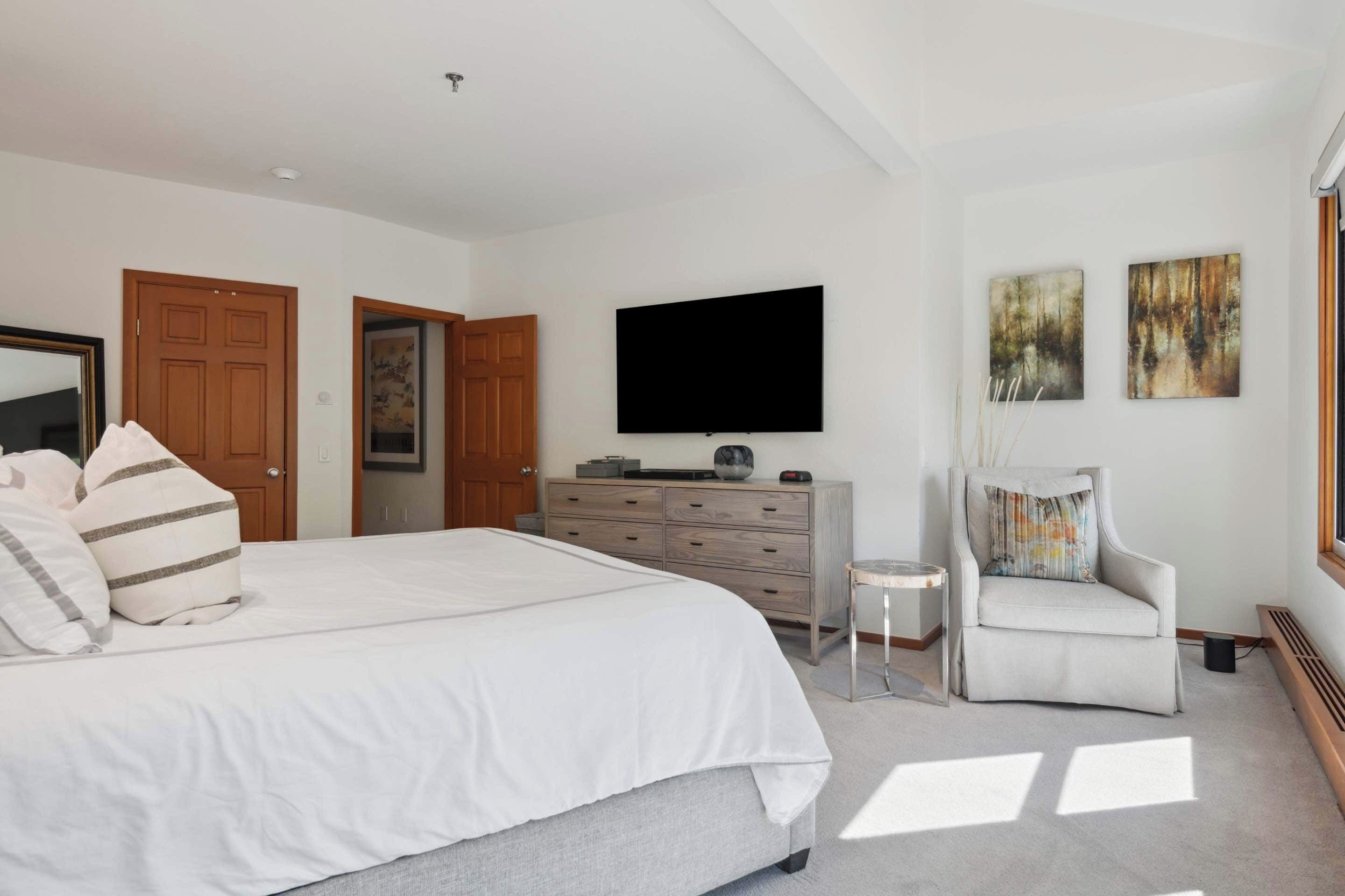 A bedroom with a large bed, a dresser, a television, and two doors.