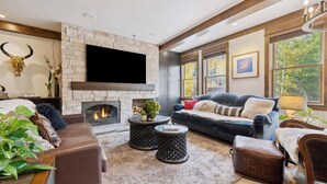 A cozy living room with a stone fireplace, leather sofas, and a large flat-screen TV. - Woodrun Place 20 Two Bedroom Residence (Snowmass)
