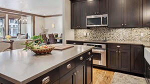 A modern kitchen with dark cabinetry, a large island, and a tiled backsplash. - Woodrun Place 20 Two Bedroom Residence (Snowmass)