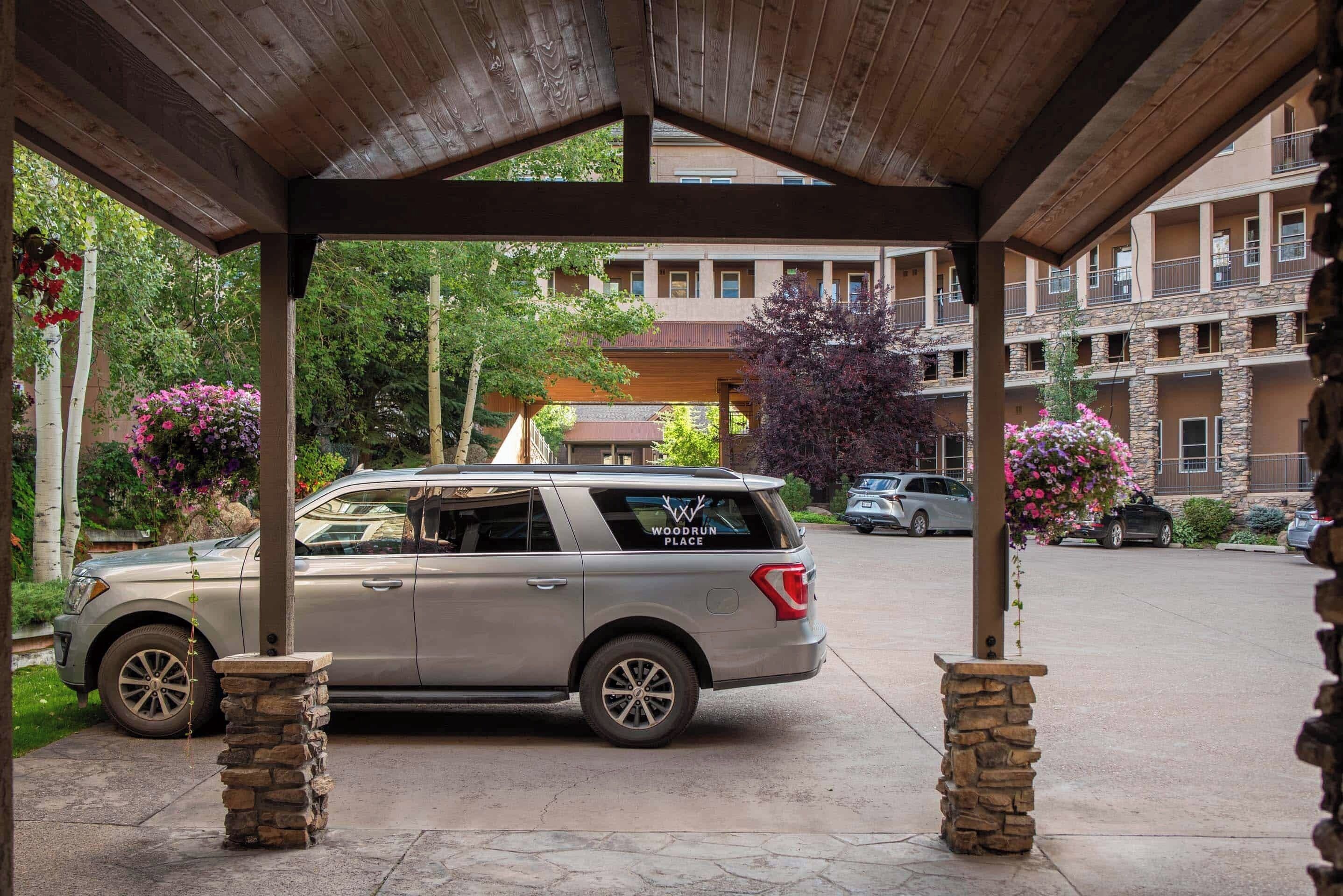 Un área de estacionamiento techada con un SUV plateado aparcado bajo una estructura de madera.