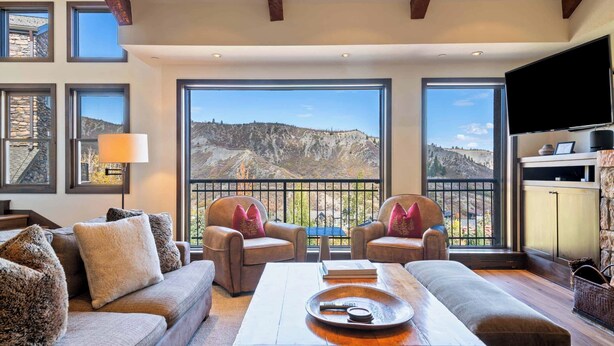 A cozy living room with a large window offering a mountain view, a flat-screen TV, and a fireplace. - Woodrun Place 26 Three Bedroom + Loft Residence (Snowmass)