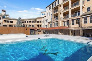 A swimming pool with clear blue water, surrounded by a multi-story building with balconies and stone accents.