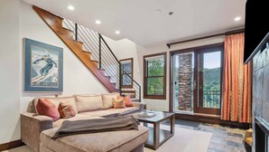 A modern living room with a staircase, a sofa, a coffee table, and a fireplace. - Woodrun Place 35 Two Bedroom Residence (Snowmass)