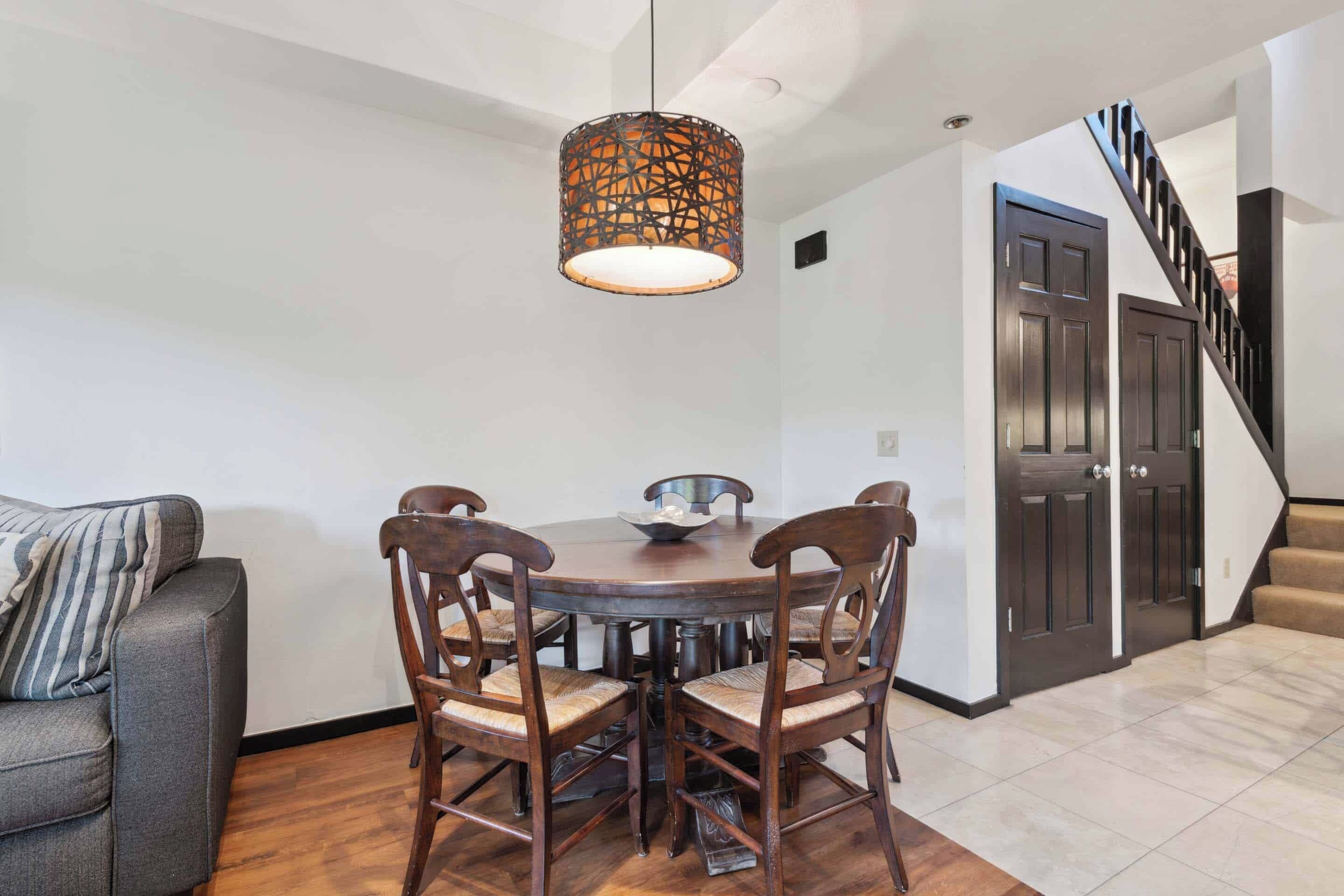 A dining area with a round table, six wooden chairs, and a hanging light fixture.