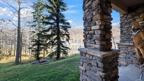 Un pilar de piedra con una estatua de una figura nativa americana, un muro de piedra y vistas de un área boscosa con un gran árbol de hoja perenne.