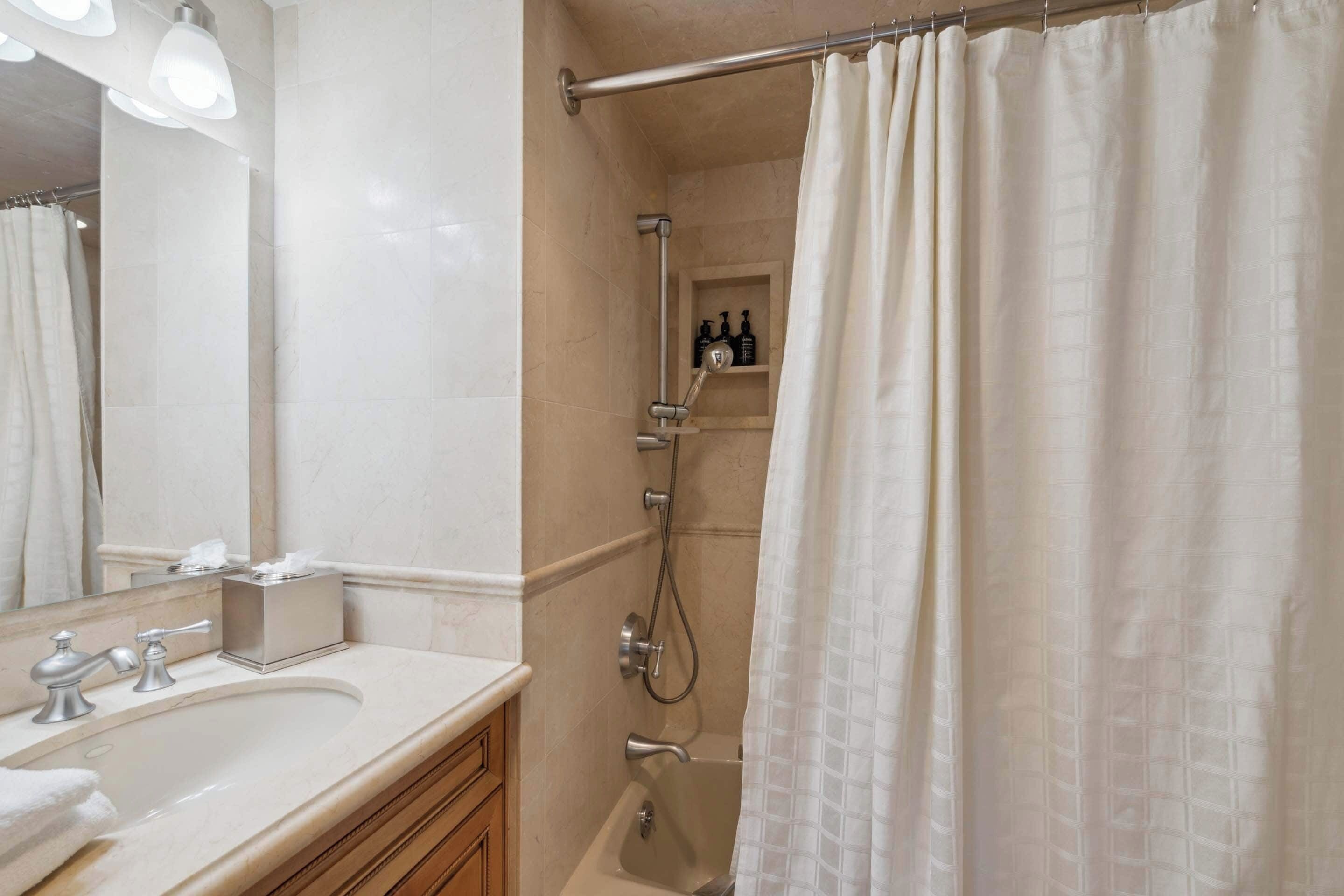 A bathroom with a sink, mirror, and shower.