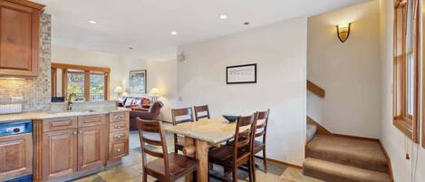 Una cocina amplia con armarios de madera, una mesa de comedor con sillas y una escalera que lleva a otro nivel.
